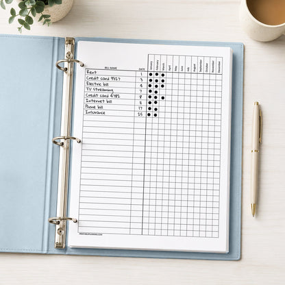 A printed Yearly Bill Payment Tracker - Printable Annual Bill Checklist (printable) page, shown with example writing, in a light blue binder on a desk with a plant, coffee, and a pen.