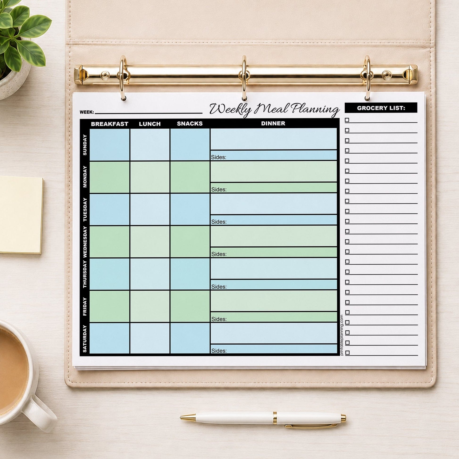 A printed Blue Green Weekly Meal Planner with Grocery List (printable page) shown in a beige binder on a table with a plant, notes, coffee, and a pen.