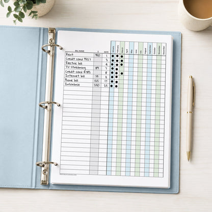 A printed Blue Green Yearly Bill Payment Tracker with Amount Column (printable) page, shown with example writing, in a light blue binder on a desk with a plant, coffee, and a pen.