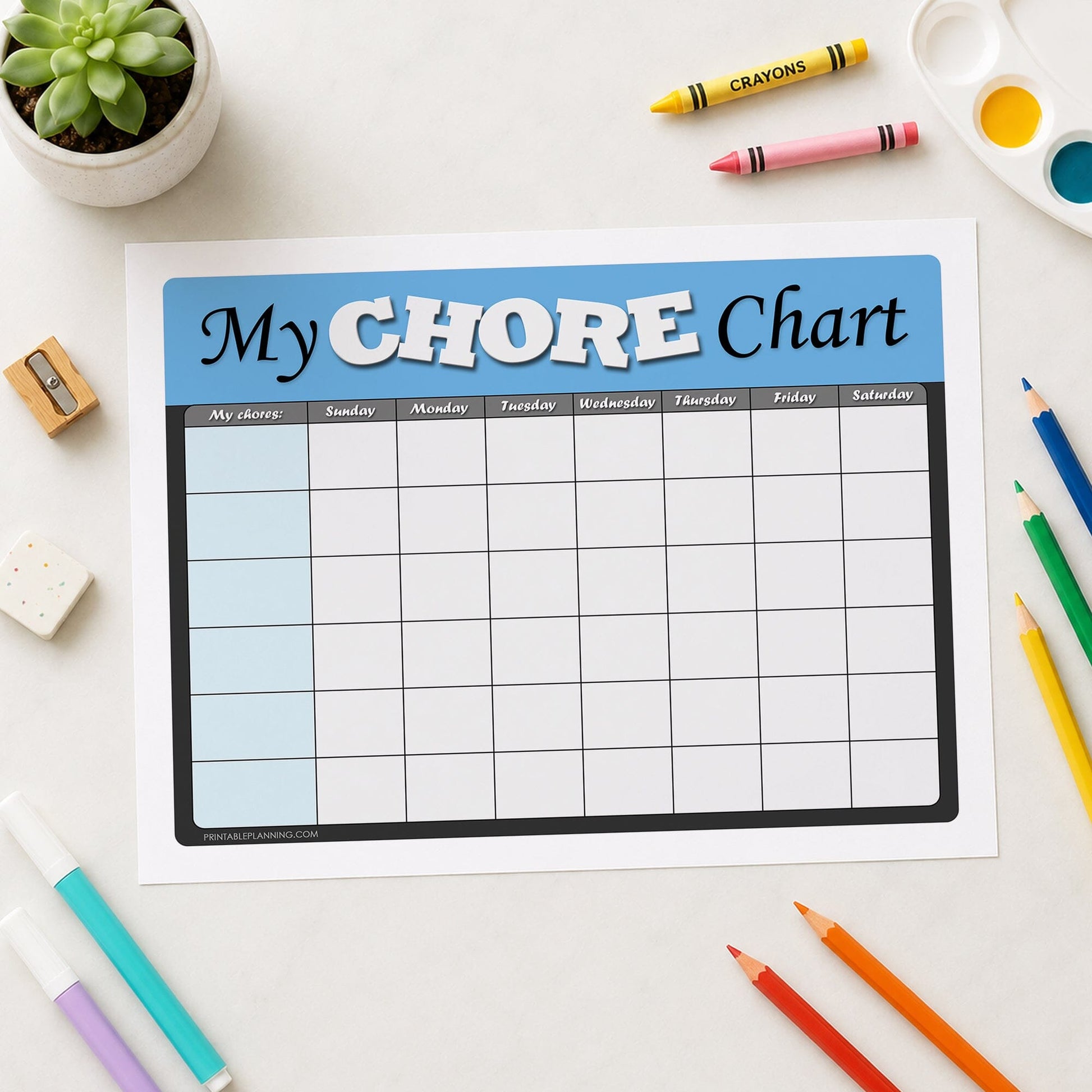 A printable 'My Chore Chart' page laid flat on a light surface, surrounded by colorful crayons, colored pencils, markers, a small succulent, and a paint palette. The chart has a blue header with white and black text and a grid for tracking chores by day.