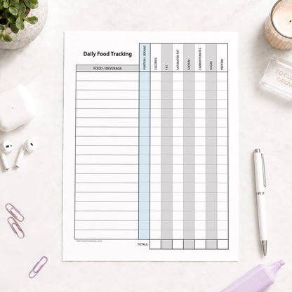 Daily Food Content Tracking Sheet (printable page) shown on a desk with earbuds, paperclips, plant, highlighter, and a pen.