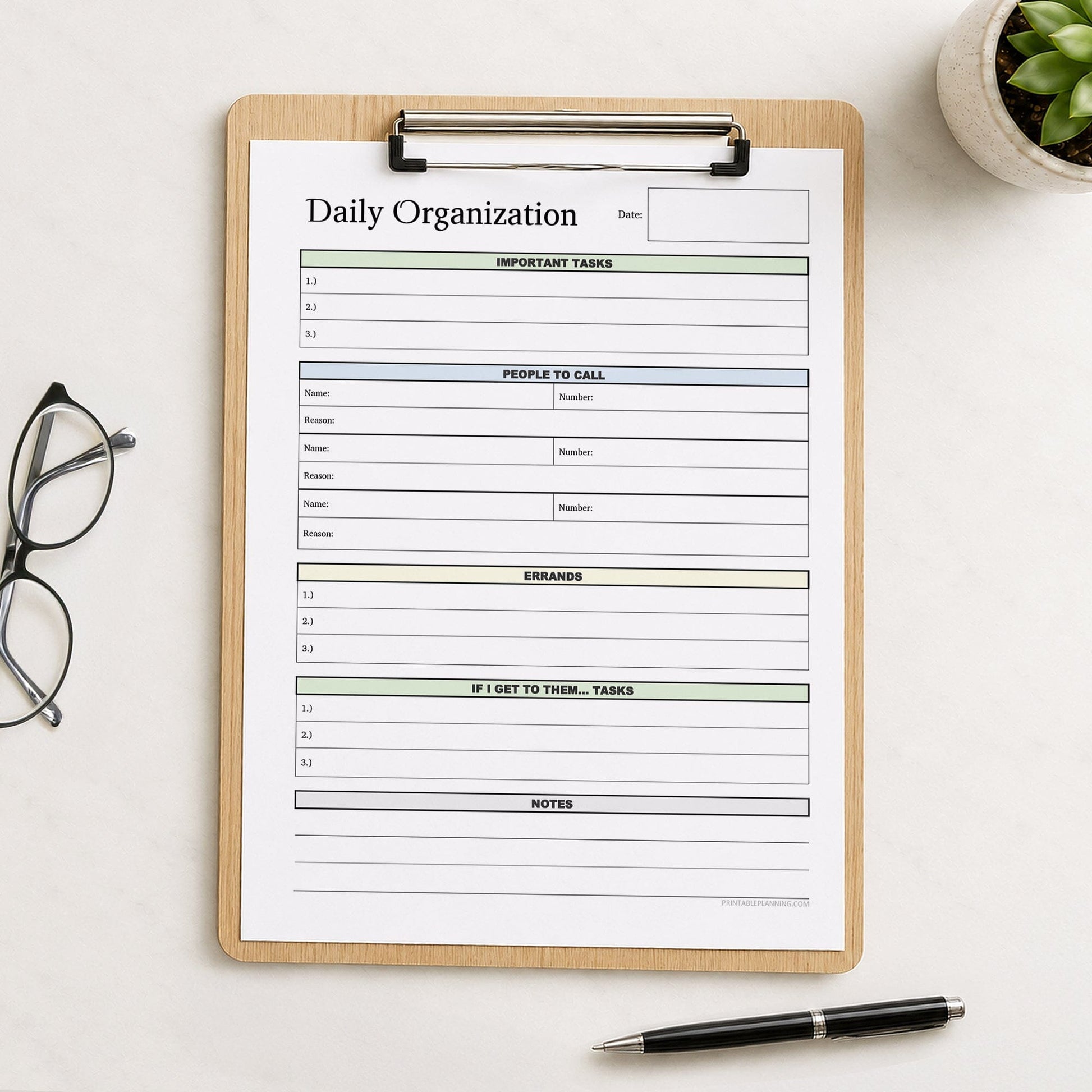 A printed Daily Planner with Priorities, Calls, Errands & Notes (printable) page shown on a wooden clipboard on a table with a plant, glasses, and a pen.