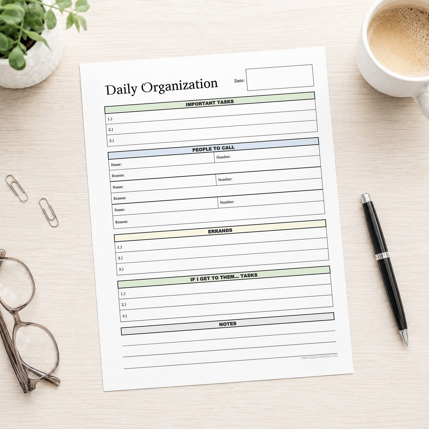 A printed Daily Planner with Priorities, Calls, Errands & Notes (printable) page shown on a desk with a plant, coffee, glasses, paperclips, and a pen.