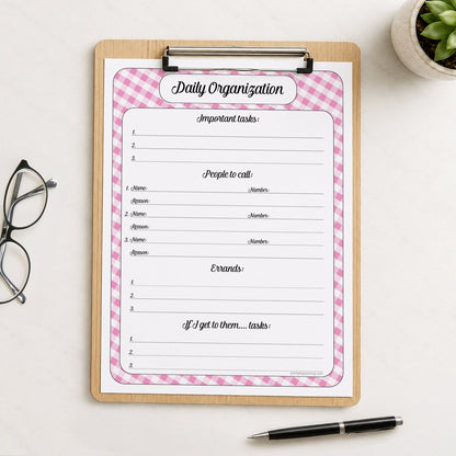 The printed pink gingham Daily Planner with Priorities, Calls & Errands (printable) page shown on a wooden clipboard on a table with a plant, glasses, and a pen.