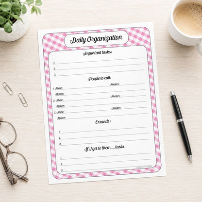 The printed pink gingham Daily Planner with Priorities, Calls & Errands (printable) page shown on a desk with a plant, glasses, paperclips, coffee, and a pen.