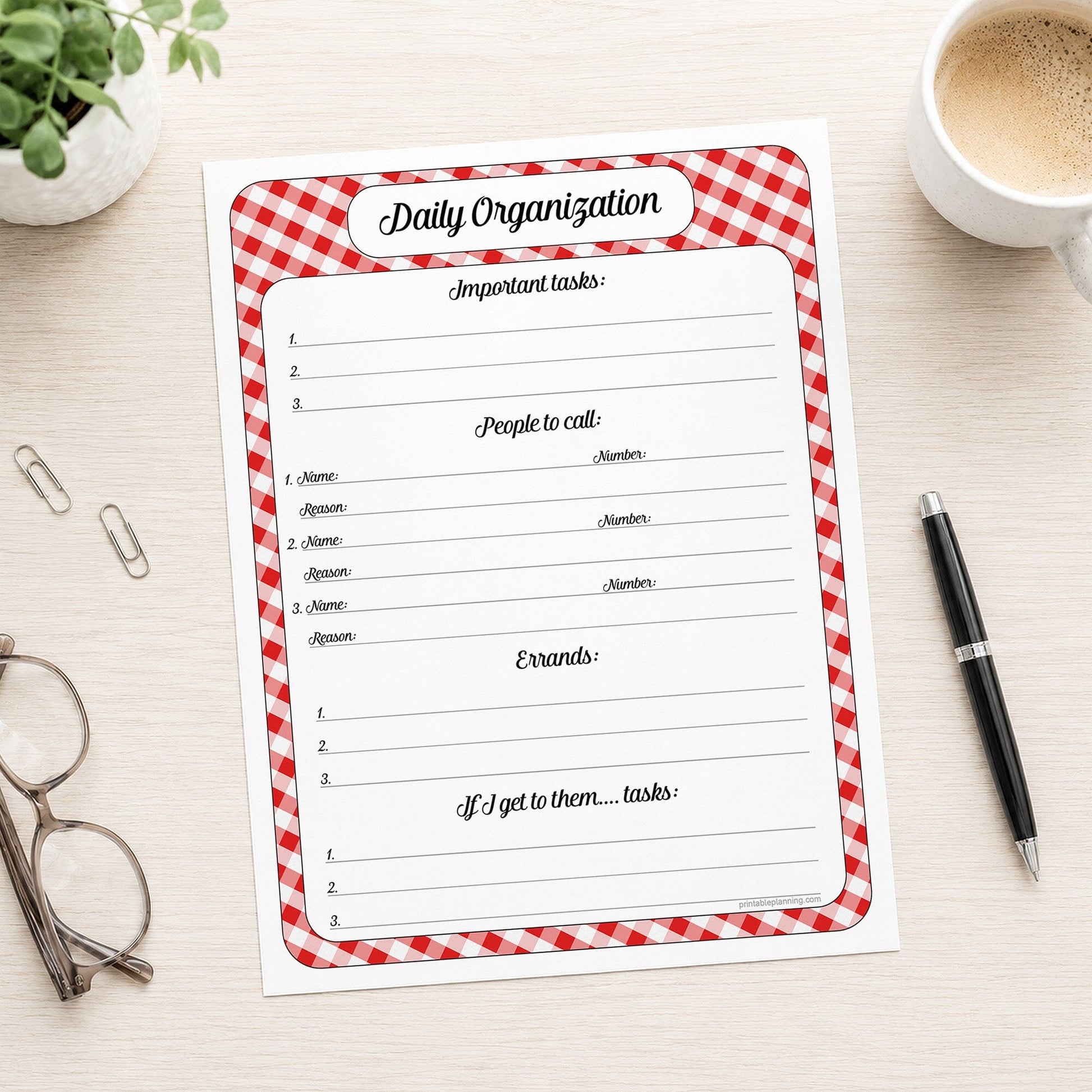 A printed red gingham Daily Priority Planner with Calls, Errands & Tasks (printable) page shown on a desk with a plant, glasses, paperclips, coffee, and a pen.