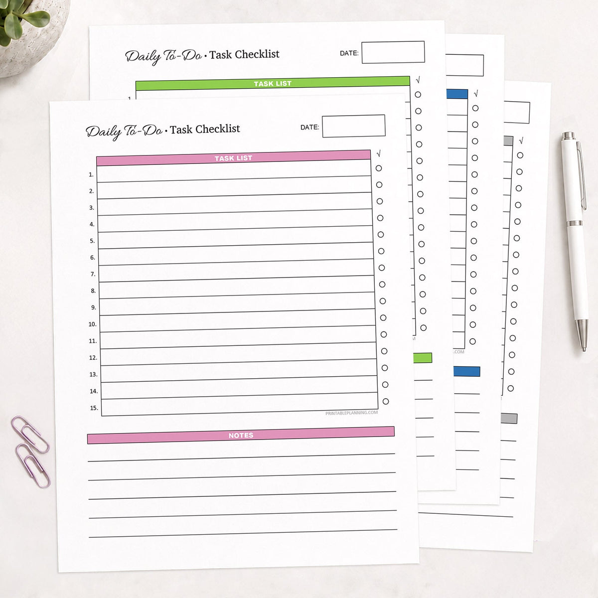 The four printed pages of the Daily To-Do List & Task Checklist Bundle, with 4 color option (printable) pages in pink, green, blue, or gray, shown on a desk with a plant, paperclips, and a pen.