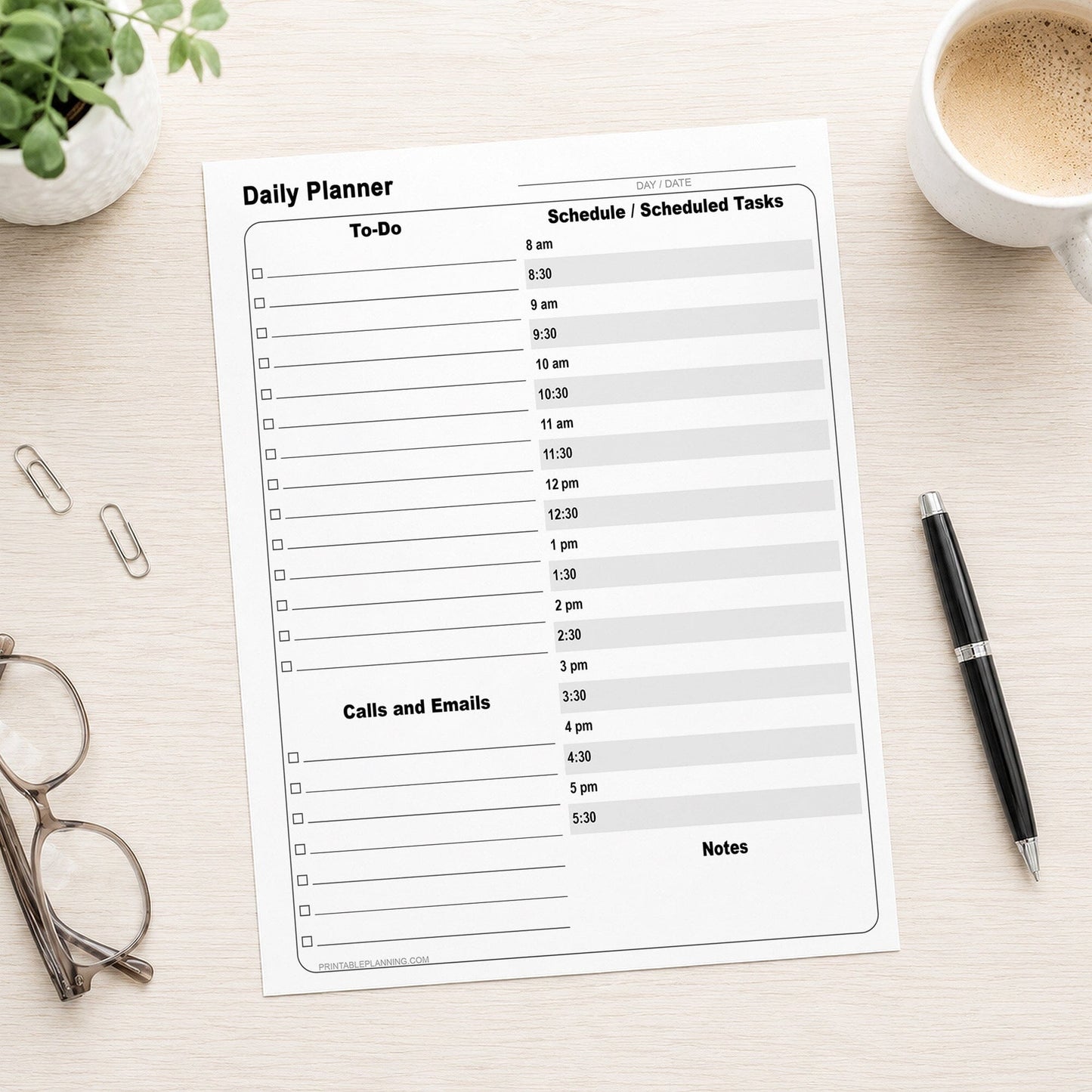 A printed Daily Work Planner with To-Do List and Schedule (printable page) laid flat on a light wood desk, surrounded by a coffee cup, pen, glasses, and paper clips. The planner has a clean white layout with gray lines and black text sections for To-Do, Calls and Emails, and Notes.