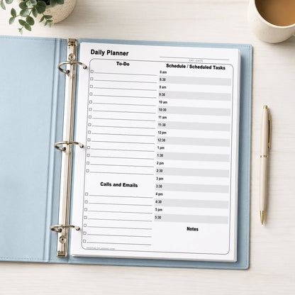 A printed Daily Work Planner with To-Do List and Schedule (printable page) shown in a light blue binder on a desk with a plant, coffee, and a pen.