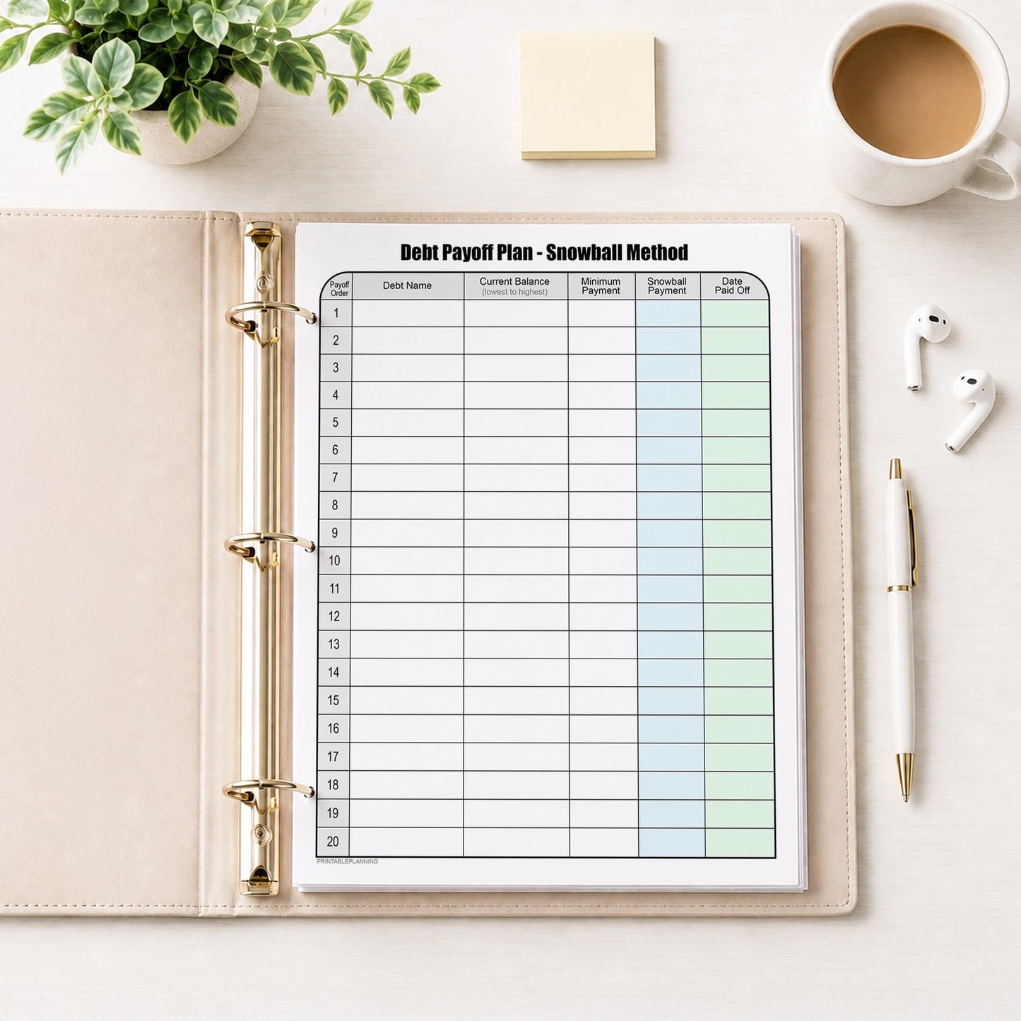 Debt Payoff Plan Chart - Debt Snowball Method (printable page) shown in a beige binder on a desk with earbuds, notes, coffee, plant, and a pen.