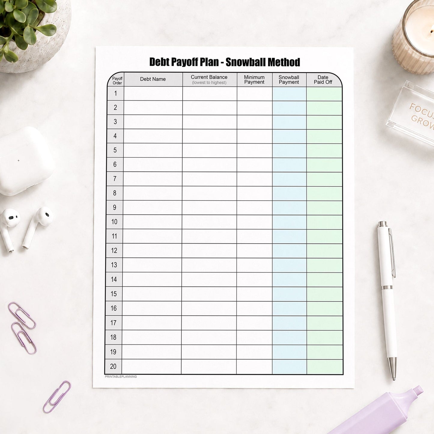 Debt Payoff Plan Chart - Debt Snowball Method (printable page) shown on a desk with earbuds, paperclips, a plant, highlighter, and a pen.