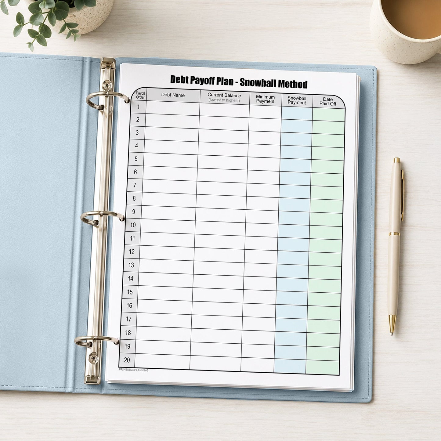 Debt Payoff Plan Chart - Debt Snowball Method (printable page) shown in a light blue binder on a desk with a plant, coffee, and a pen.