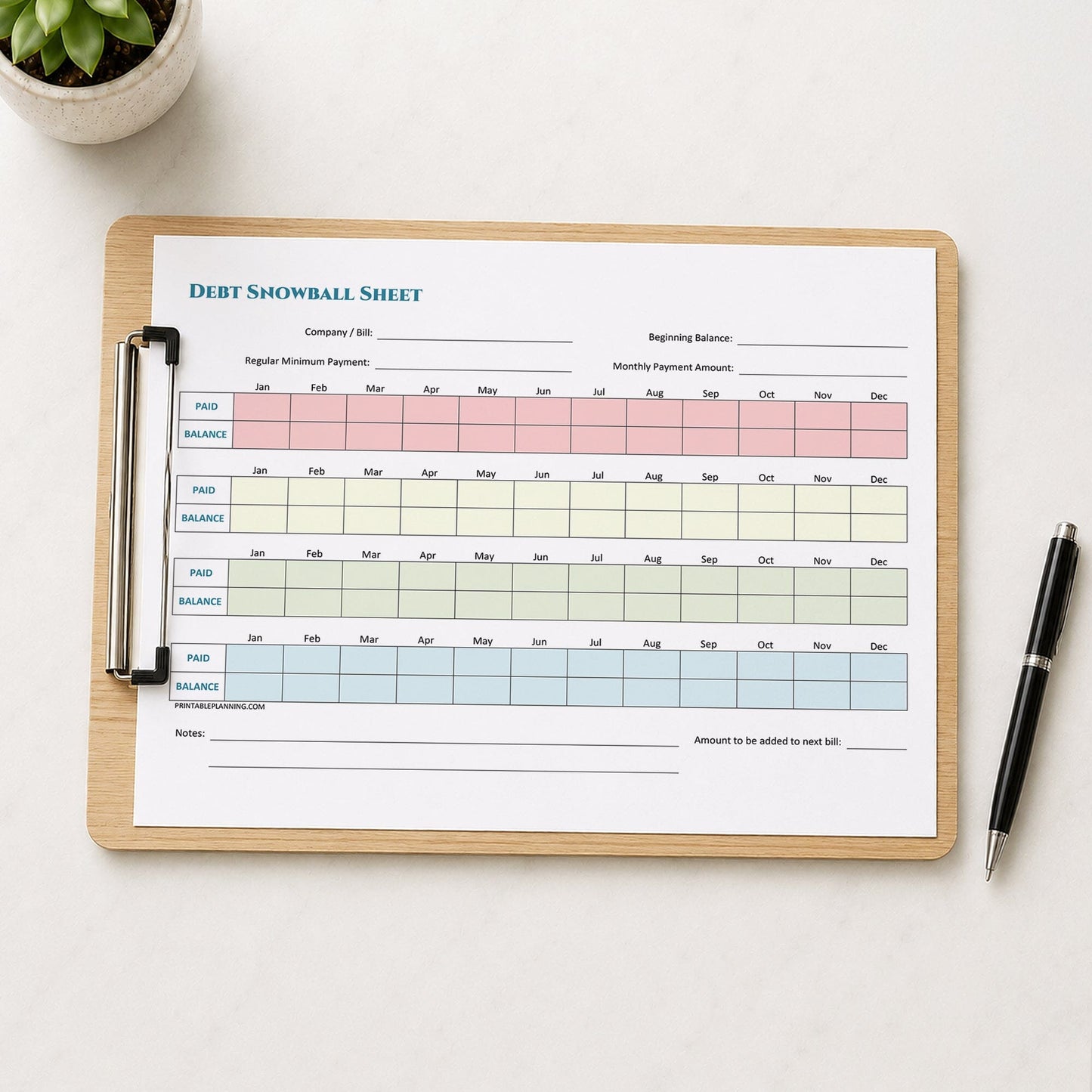 A printed Debt Snowball Tracker (printable) page shown on a wooden clipboard on a table with a plant and a pen.