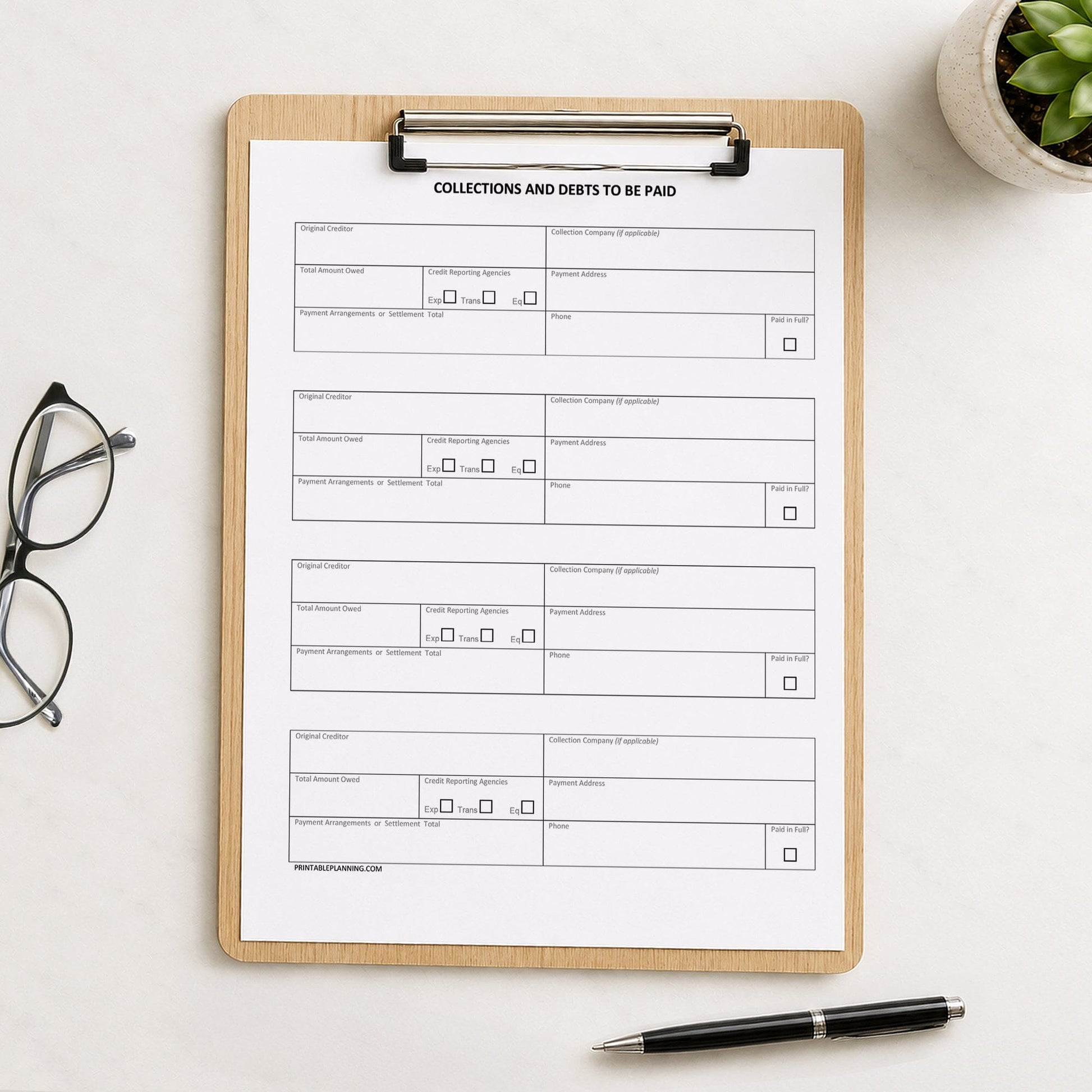 A printed Debt & Collections Tracker for Creditors and Payment Arrangements page shown on a wooden clipboard on a table with glasses, a plant, and a pen.