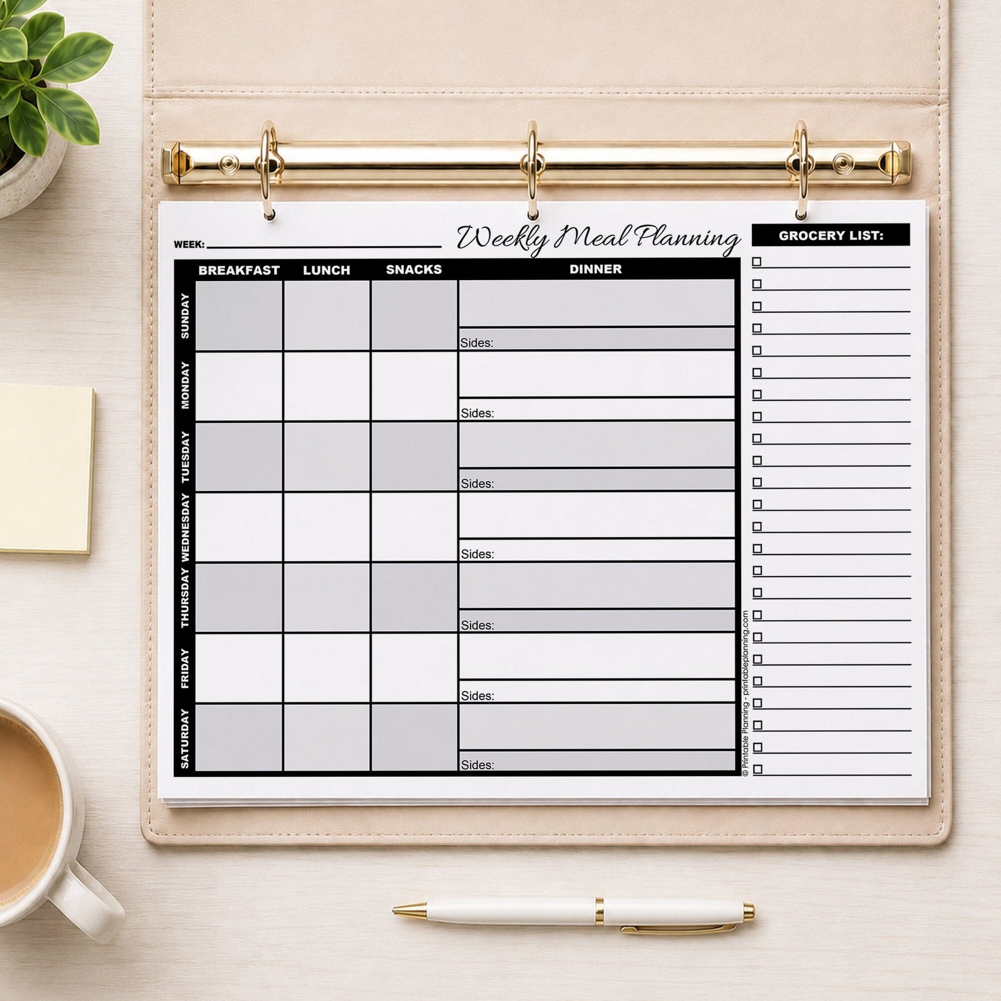 A printed Grayscale Weekly Meal Planner with Grocery List (printable page) shown in a beige binder on a table with a plant, coffee, sticky notes, and a pen.
