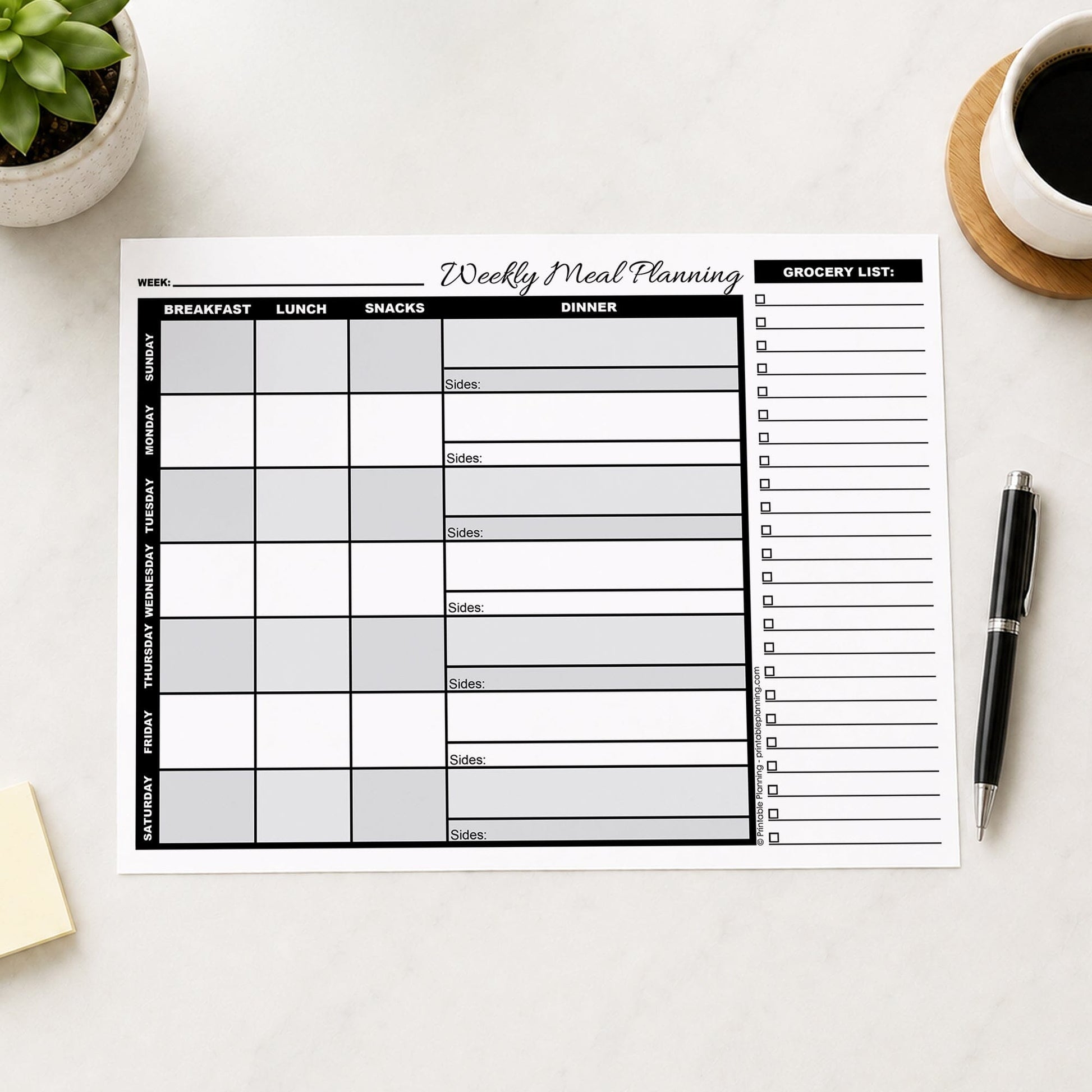A printed Grayscale Weekly Meal Planner with Grocery List (printable page) shown on a table with a plant, coffee, sticky notes, and a pen.