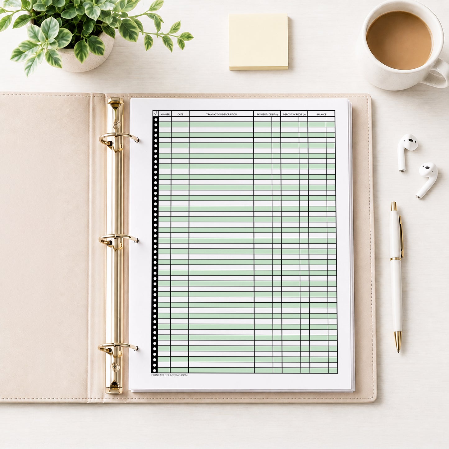 Green Printable Check Register - Full-Page Transaction Tracker shown in an open beige binder on a desk with earbuds, notes, coffee, a plant, and a pen.