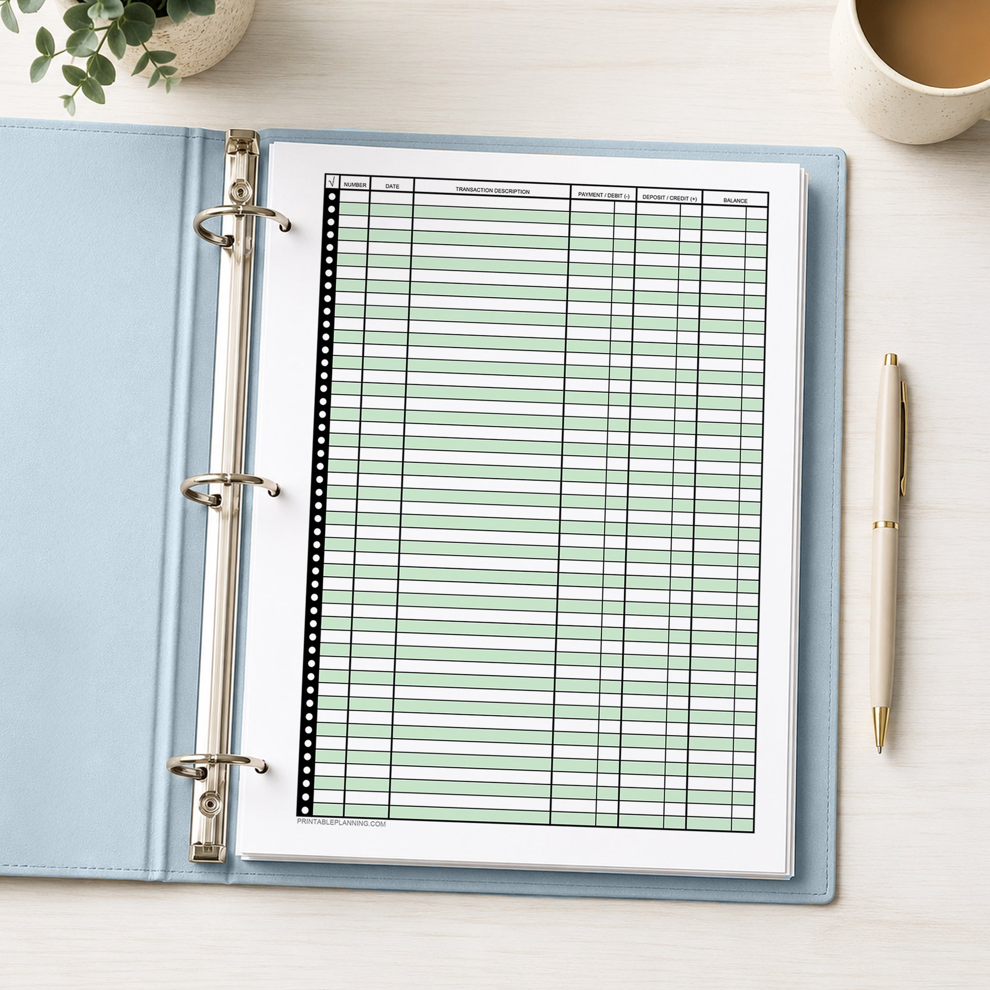 Green Printable Check Register - Full-Page Transaction Tracker shown in an open light blue binder on a desk with a plant, coffee, and a pen.