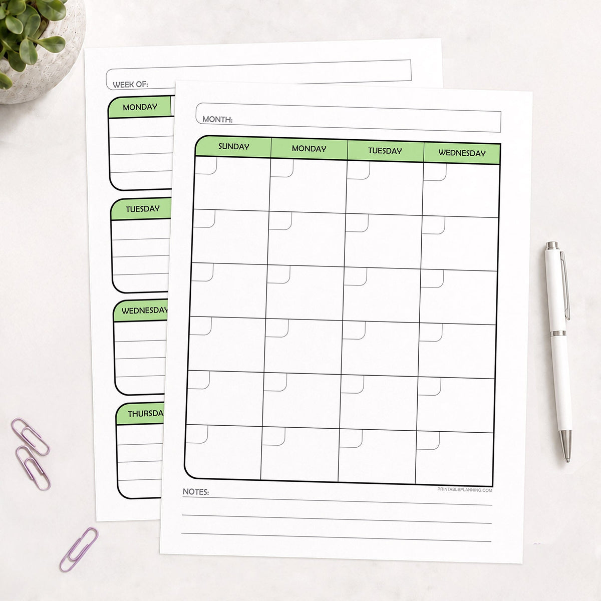 The printed Green Undated Monthly & Weekly Planner (printable) Pages shown on a desk with a plant, paperclips, and a pen.
