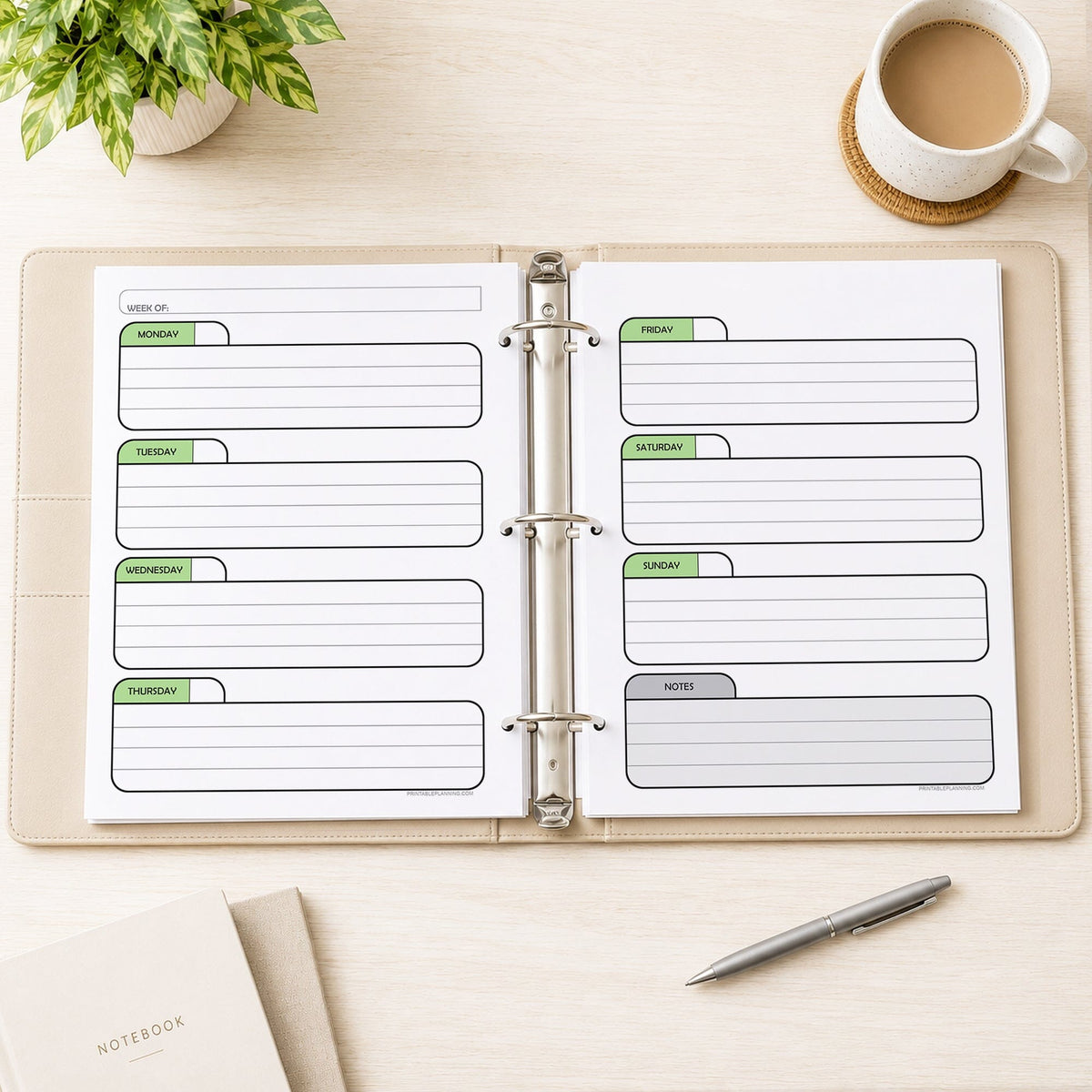 The printed Green Undated Weekly Planner (printable) Pages shown in an open beige binder as facing pages, on a desk with a plant, coffee, notebooks, and a pen.