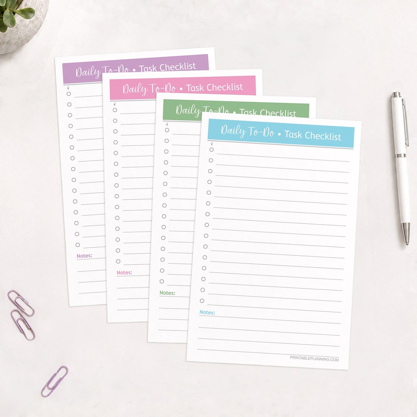 Printed copies of the printable Half-Page Daily To-Do List & Task Checklist Bundle in 4 Soft Colors, shown on a table with a plant, paperclips, and a pen.