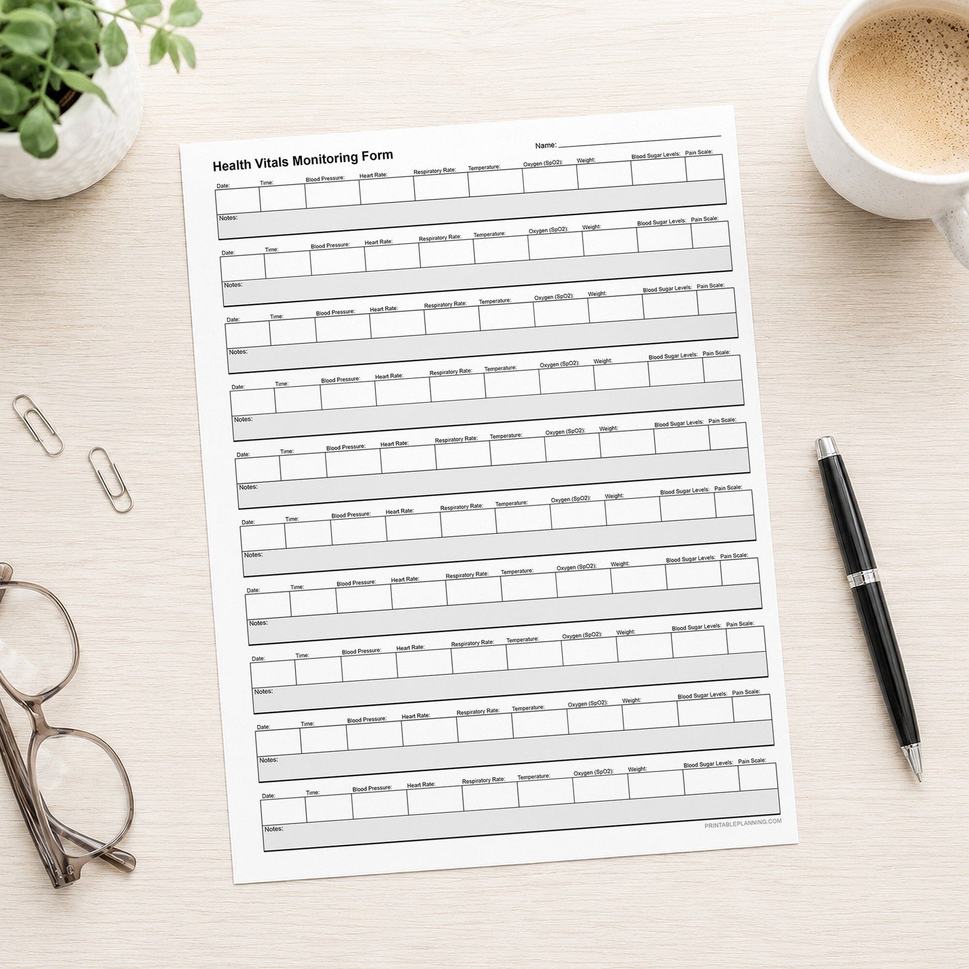 A printed Health Vitals Tracker for Caregivers (printable page) shown on a desk with a plant, glasses, paperclips, coffee, and a pen.