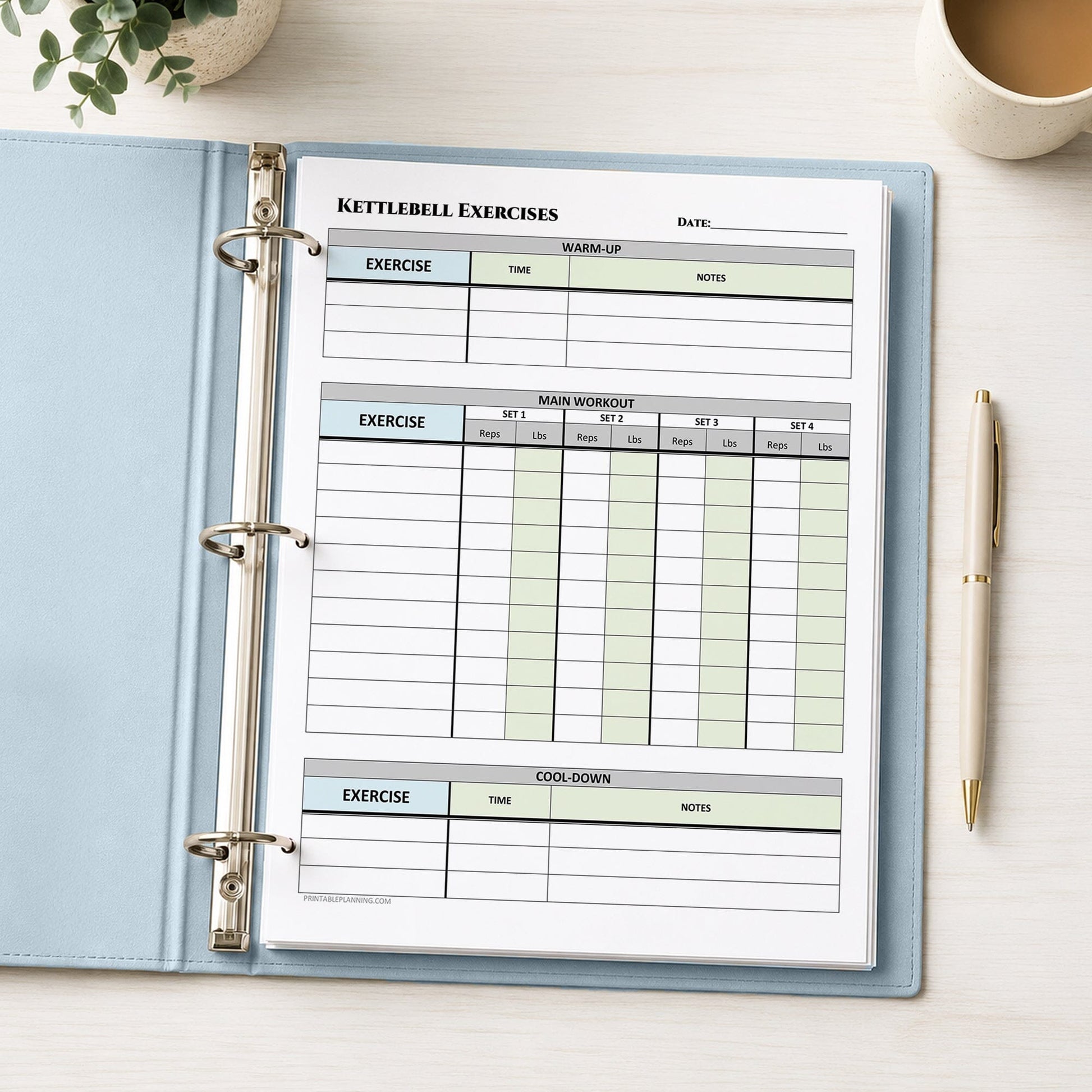 A light blue ring binder notebook open on a light desk, showing a printed 'Kettlebell Exercises' tracking sheet with tables for warm-up, main workout, and cool-down. A pen, plant, and cup are visible around it.