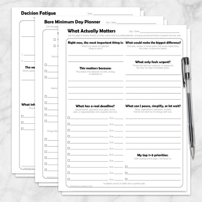 Low-Energy Day Planner Printable Bundle, including the What Actually Matters Priority Worksheet, Bare Minimum Day Planner - Printable Page,  and the Decision Fatigue Printable Worksheet, shown on a marble surface with a pen.