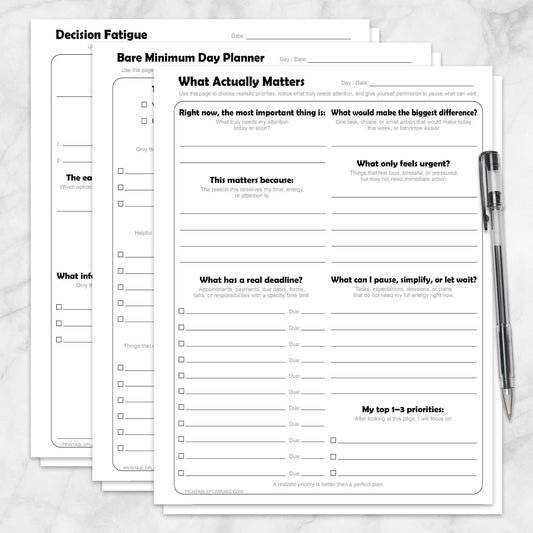 Low-Energy Day Planner Printable Bundle, including the What Actually Matters Priority Worksheet, Bare Minimum Day Planner - Printable Page,  and the Decision Fatigue Printable Worksheet, shown on a marble surface with a pen.