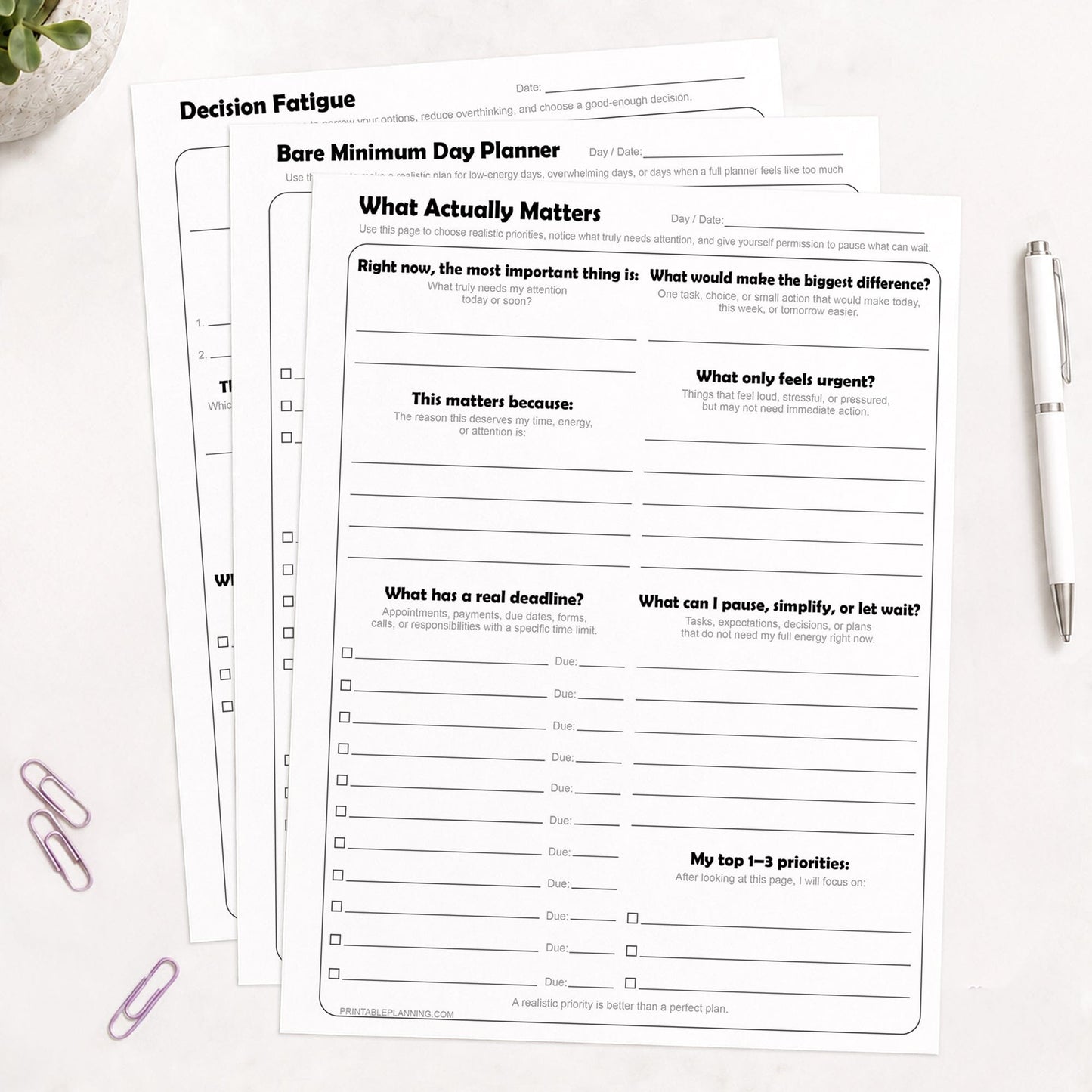 Low-Energy Day Planner Printable Bundle, including the What Actually Matters Priority Worksheet, Bare Minimum Day Planner - Printable Page,  and the Decision Fatigue Printable Worksheet, shown on light desk with a plant, paperclips, and a pen.