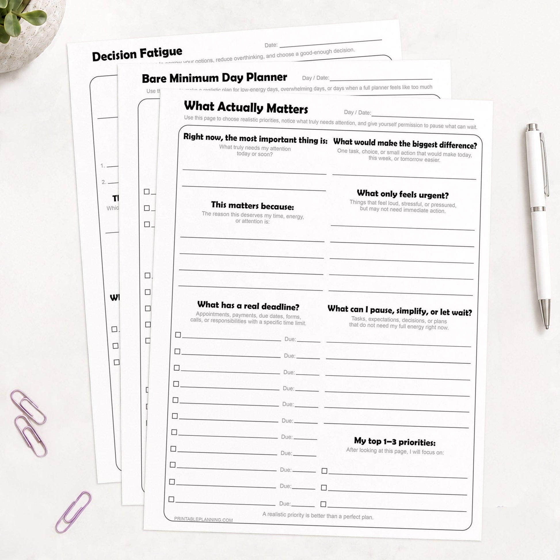 Low-Energy Day Planner Printable Bundle, including the What Actually Matters Priority Worksheet, Bare Minimum Day Planner - Printable Page,  and the Decision Fatigue Printable Worksheet, shown on light desk with a plant, paperclips, and a pen.