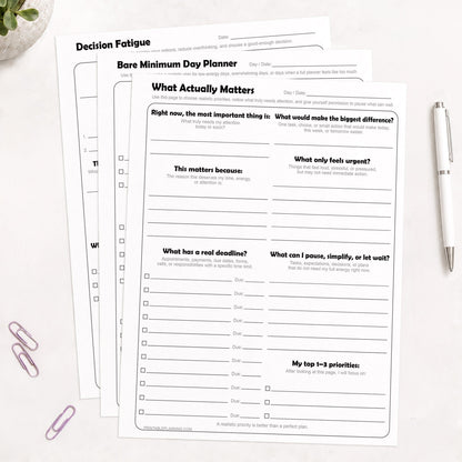 Low-Energy Day Planner Printable Bundle, including the What Actually Matters Priority Worksheet, Bare Minimum Day Planner - Printable Page,  and the Decision Fatigue Printable Worksheet, shown on light desk with a plant, paperclips, and a pen.