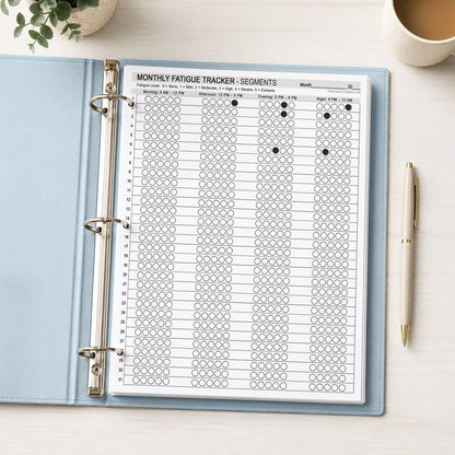 Monthly Fatigue Tracker Segments printable with morning afternoon evening and night severity circles, shown with example writing in a light blue binder on a desk with a plant, coffee, and a pen.