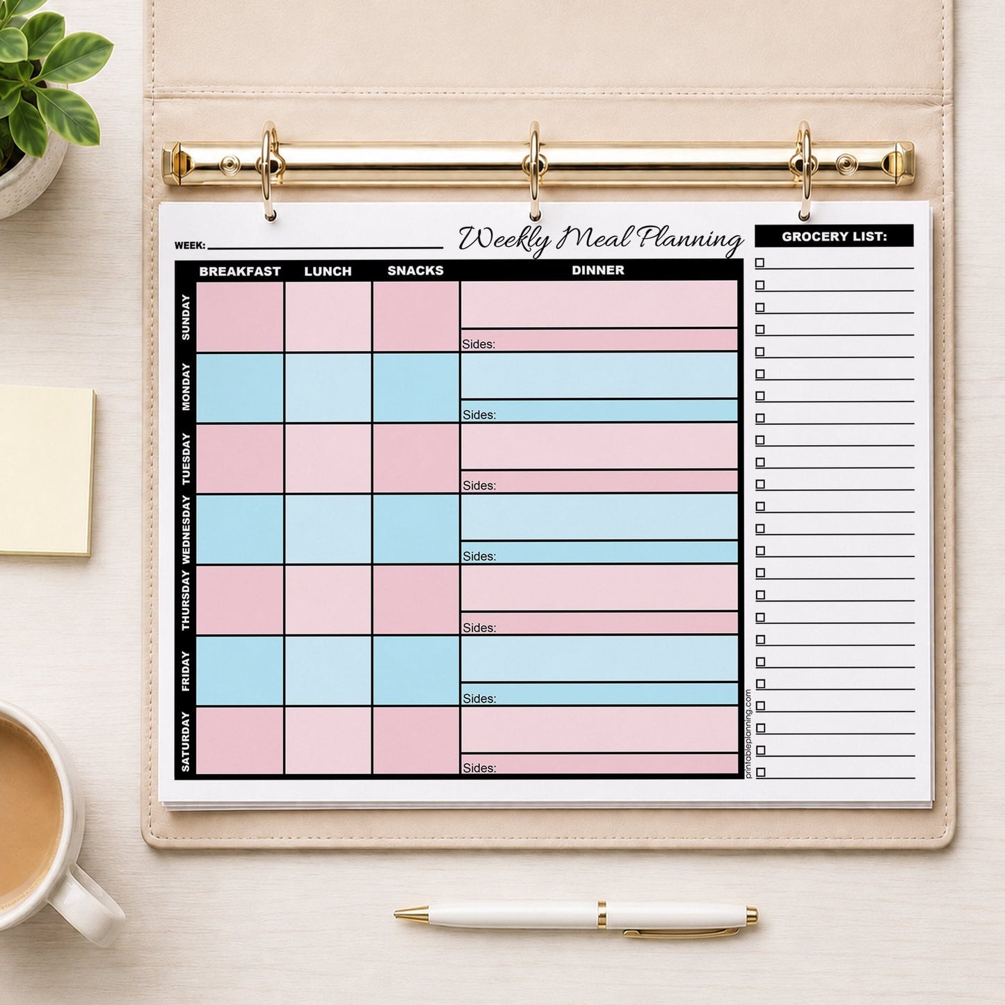 A printed Pink Blue Weekly Meal Planner with Grocery List (printable page) shown in a beige binder on a desk with a plant, notes, coffee, and a pen.
