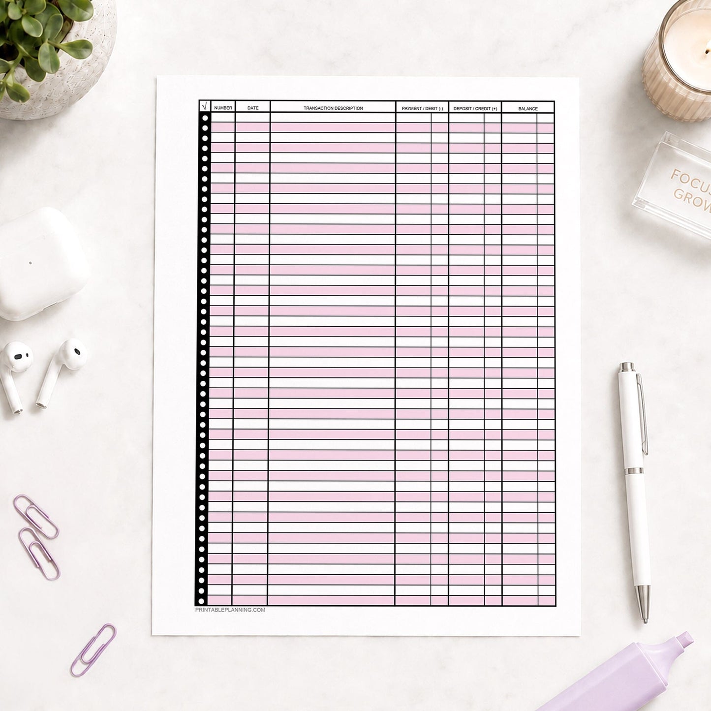 Pink Printable Check Register - Full-Page Transaction Tracker shown on a light desk with earbuds, paperclips, highlighter, plant, and a pen.