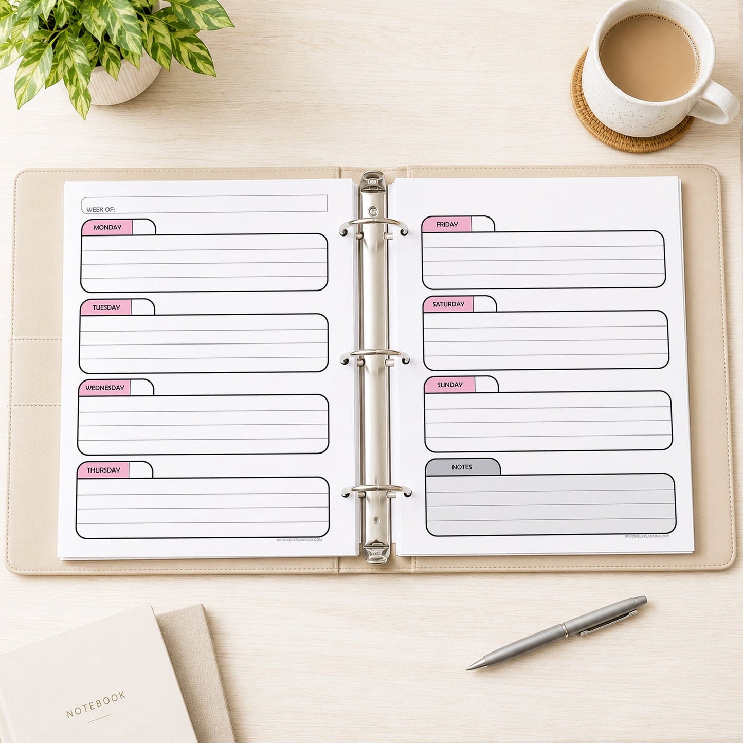 The printed Pink Undated Weekly Planner (printable) Pages shown in an open beige binder showing facing pages, on a desk with a plant, coffee, notebooks, and a pen.