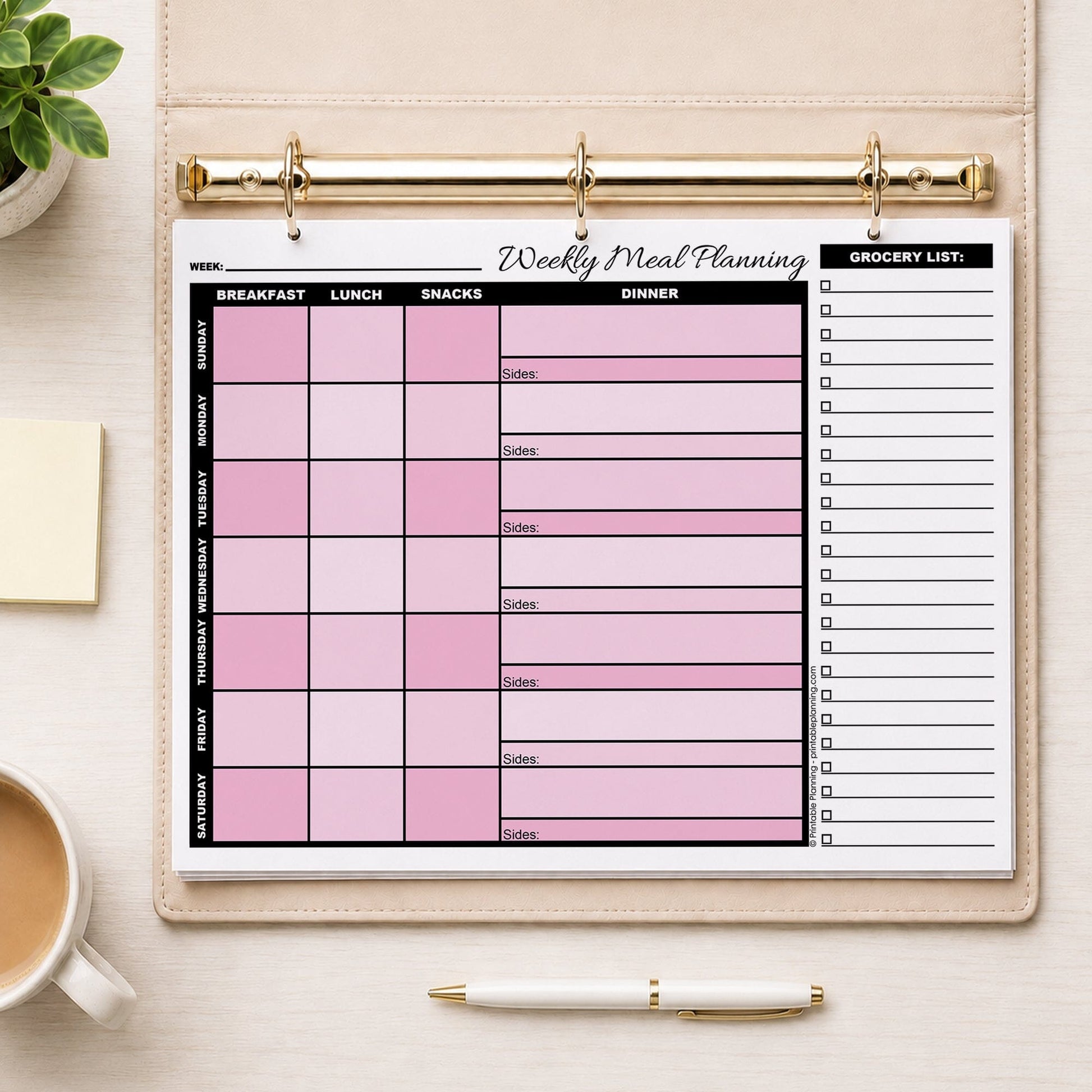 A printed Pink Weekly Meal Planner with Grocery List (printable page) shown in a beige binder on a table with a plant, sticky notes, coffee, and a pen.