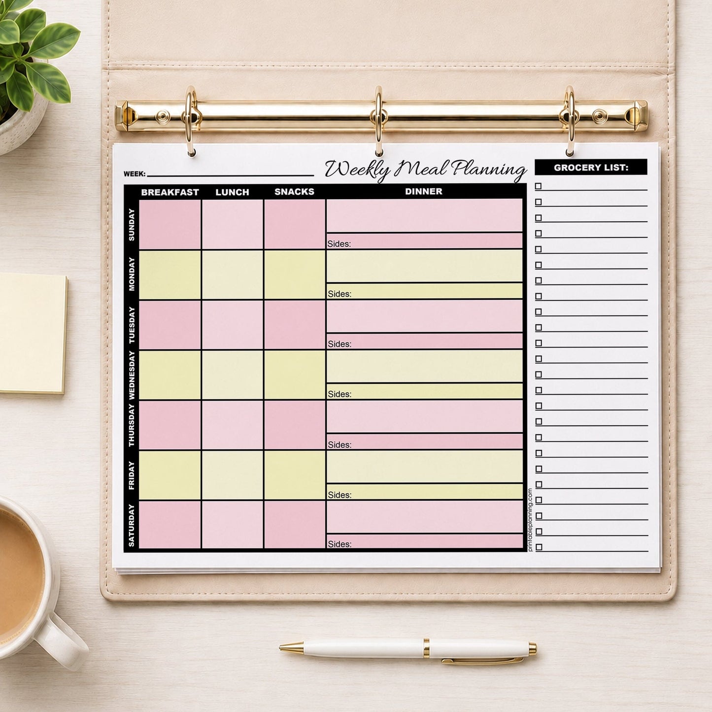 A printed Pink Yellow Weekly Meal Planner with Grocery List (printable page) in a beige ring binder, styled on a light wood desk with a coffee cup, sticky notes, a pen, and a small plant.