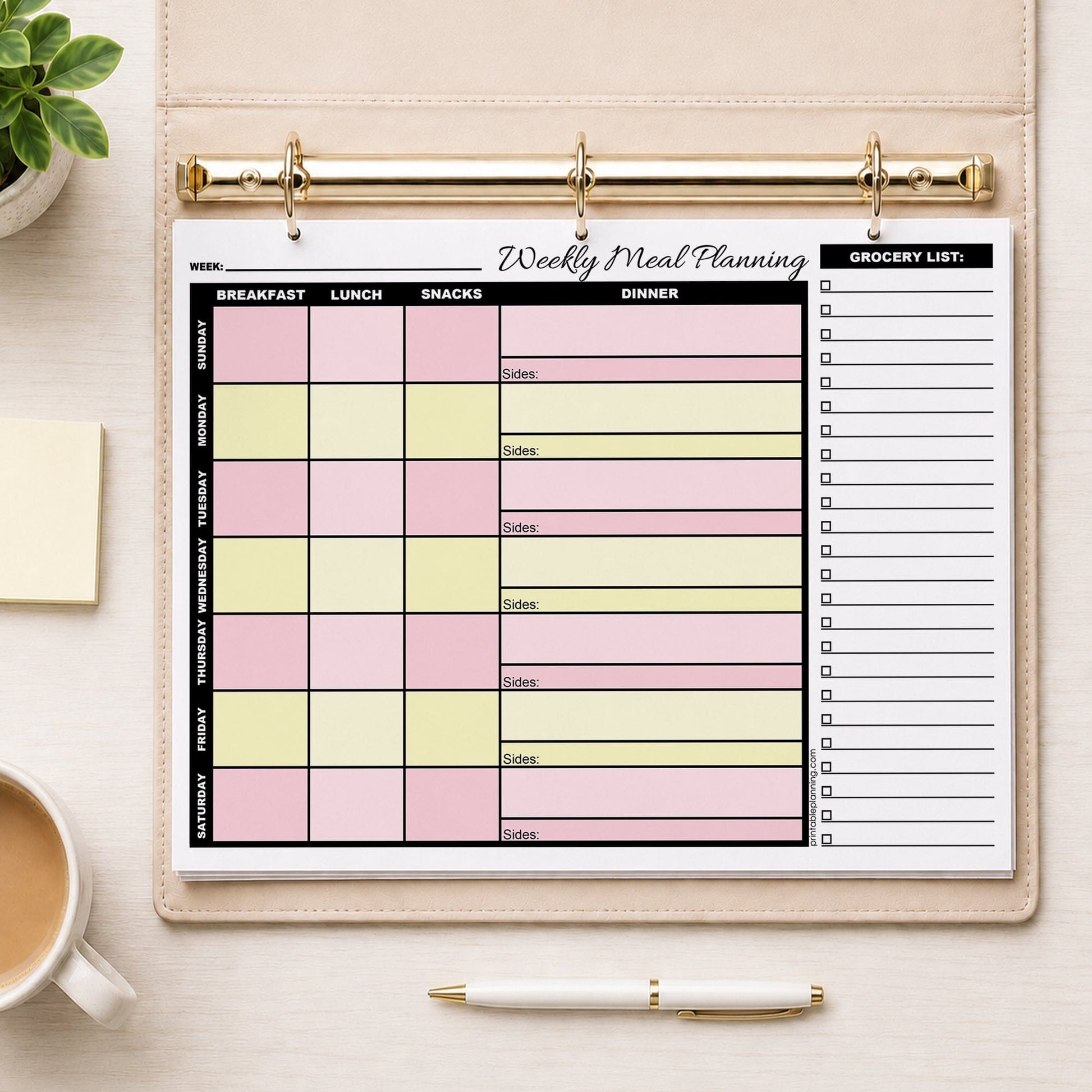 A printed Pink Yellow Weekly Meal Planner with Grocery List (printable page) in a beige ring binder, styled on a light wood desk with a coffee cup, sticky notes, a pen, and a small plant.