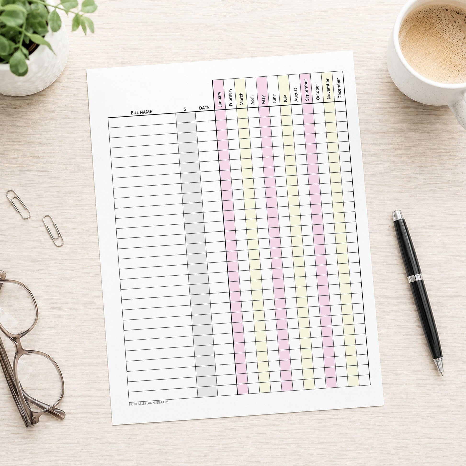 Pink Yellow Yearly Bill Payment Tracker with Amount Column (printable page) shown on a desk with a plant, glasses, paperclips, coffee, and a pen.