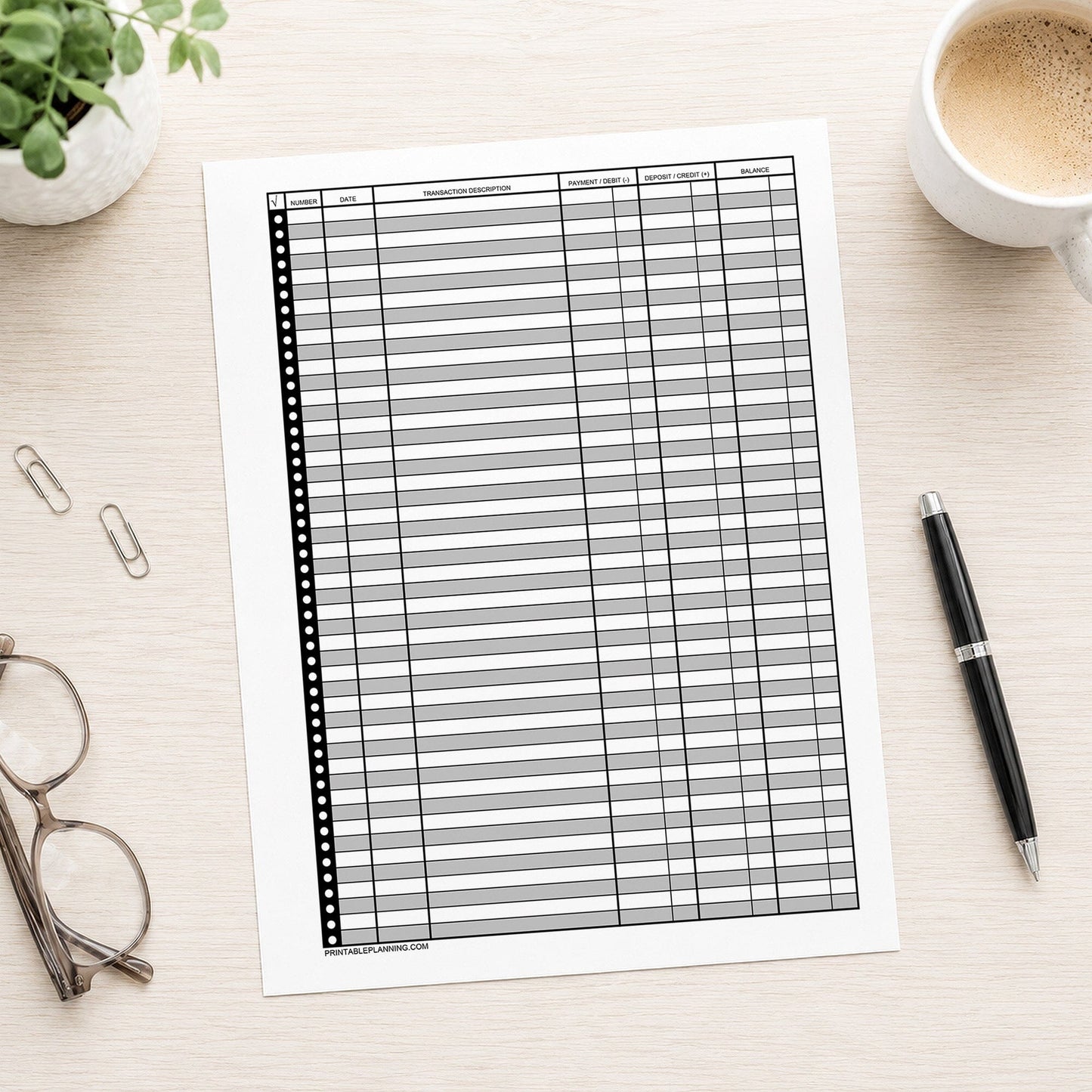 Printable Check Register - Full-Page Financial Transaction Tracker displayed on a light wood desk surrounded by a coffee cup, glasses, paper clips, and a pen.