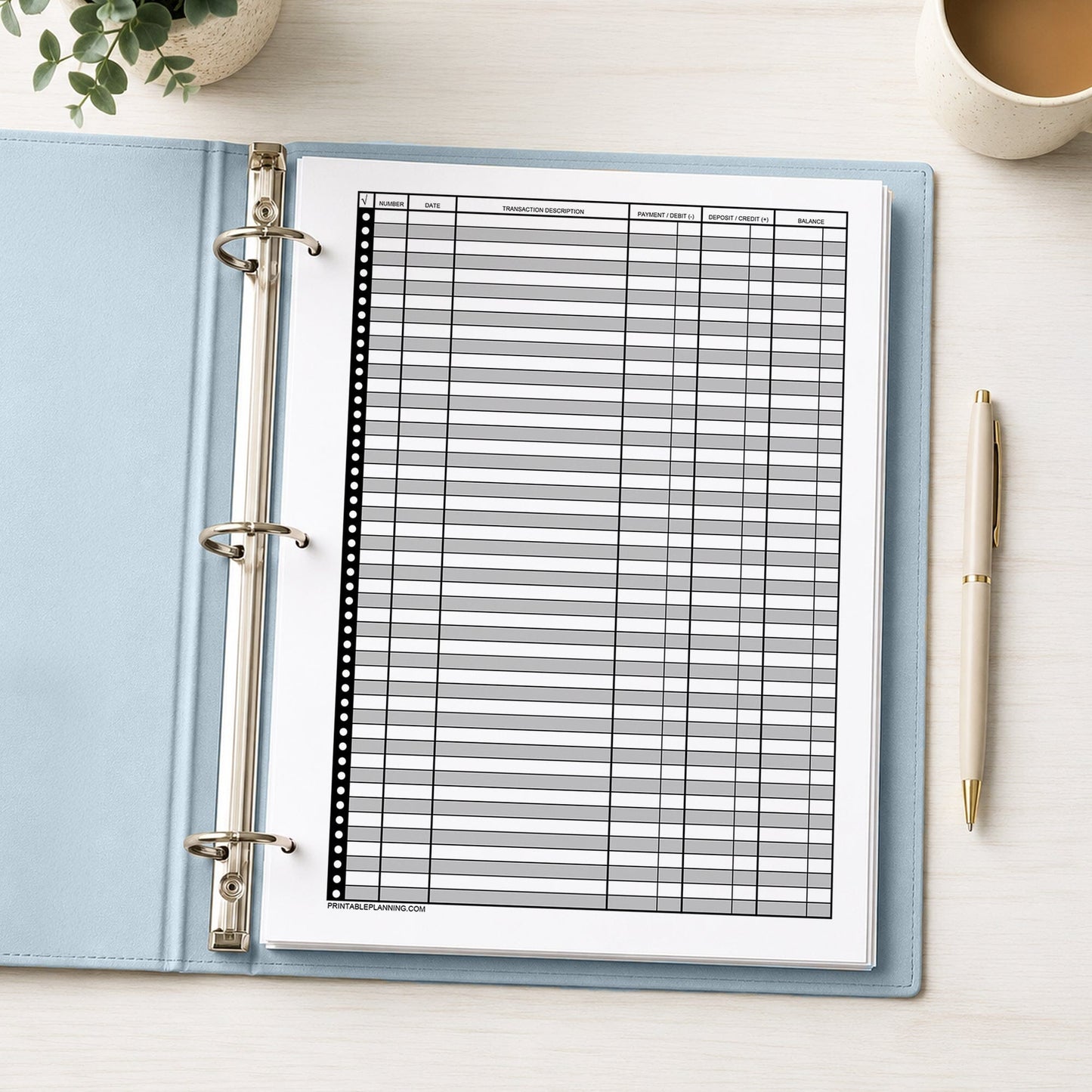Printable Check Register - Full-Page Financial Transaction Tracker shown in a light blue binder on a desk with a plant, coffee, and a pen.