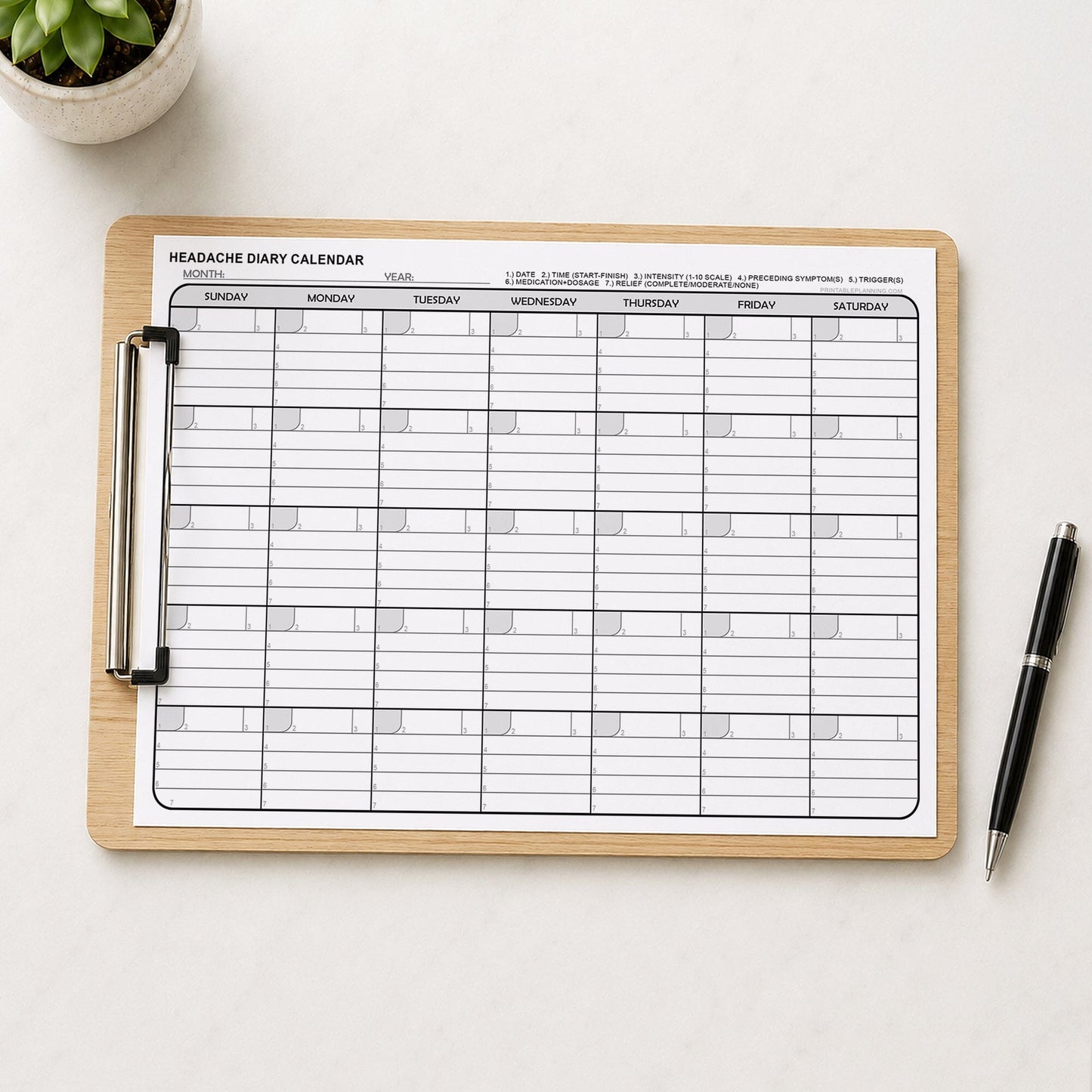 Printable Headache Diary Calendar - Monthly Migraine Tracker PDF shown on a clipboard on a desk with a plant and a pen.