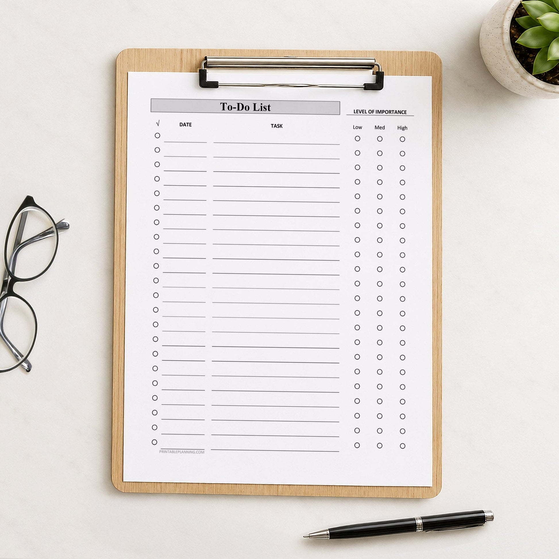 A wooden clipboard holding a printed Priority To-Do List with Low Medium High Importance - Printable PDF sheet, styled on a light desk surface with eyeglasses, a pen, and a small potted succulent nearby.