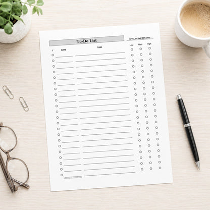 A printed Priority To-Do List with Low Medium High Importance - Printable PDF with columns for date, task, and priority, styled in a flat-lay on a light wood desk with a coffee cup, glasses, paper clips, and a pen.