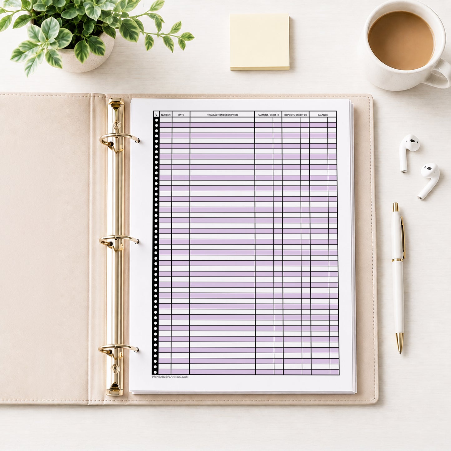 Purple Printable Check Register - Full-Page Transaction Tracker shown in an open beige binder on a desk with a plant, earbuds, coffee, notes, and a pen.