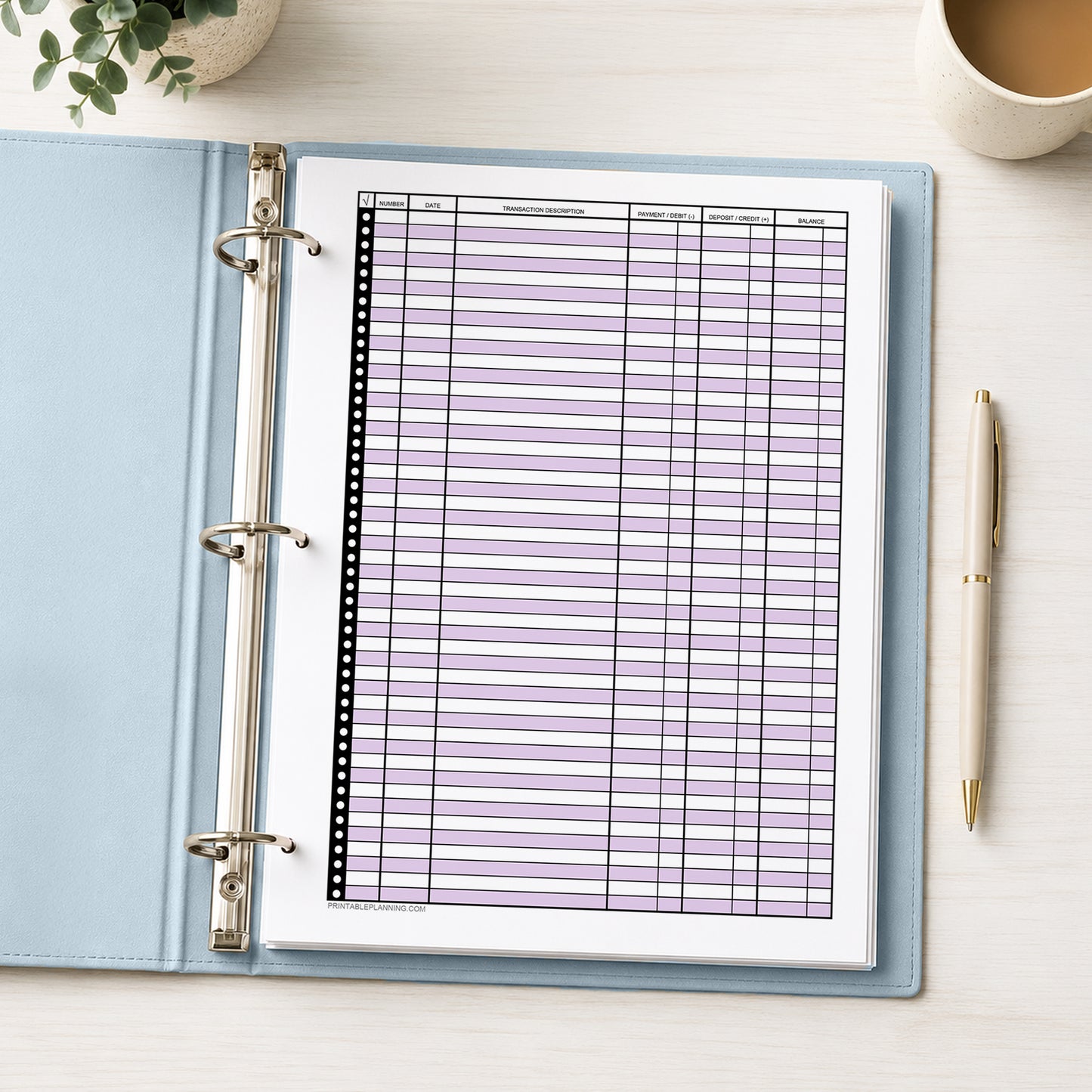 Purple Printable Check Register - Full-Page Transaction Tracker shown in a light blue binder on a desk with a plant, coffee, and a pen.
