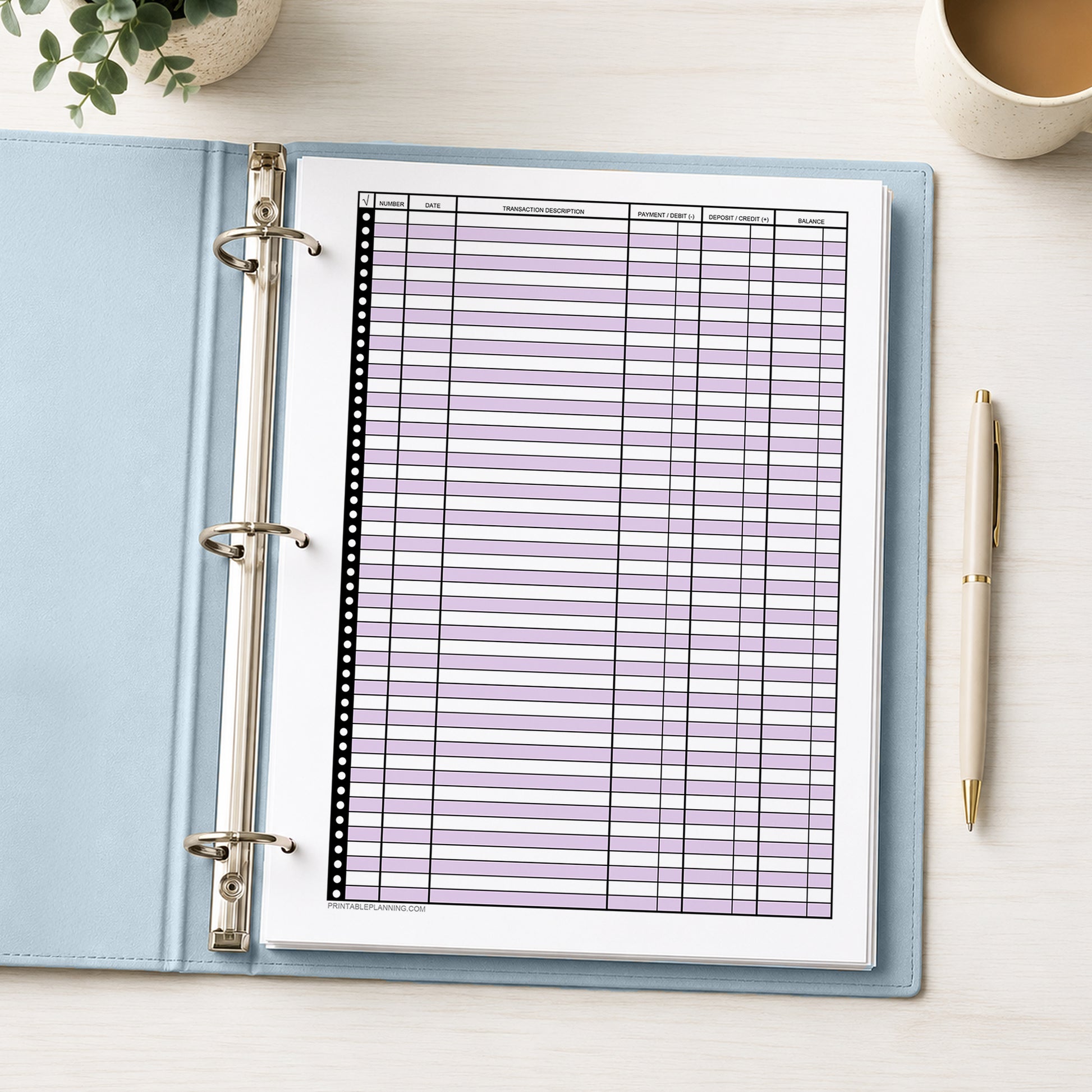 Purple Printable Check Register - Full-Page Transaction Tracker shown in a light blue binder on a desk with a plant, coffee, and a pen.