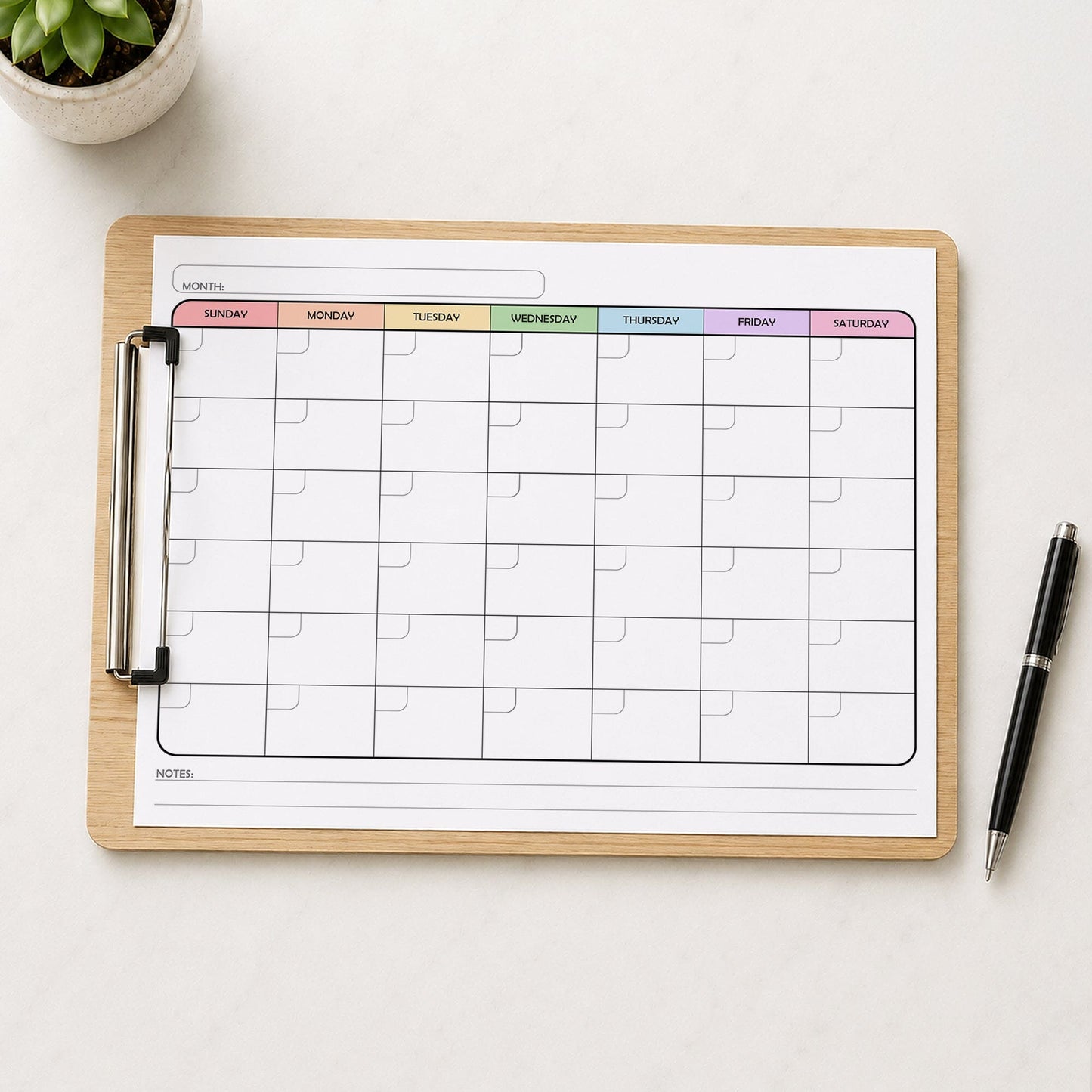 A printed rainbow undated monthly calendar (printable) page shown on a wooden clipboard on a table with a plant and a pen.