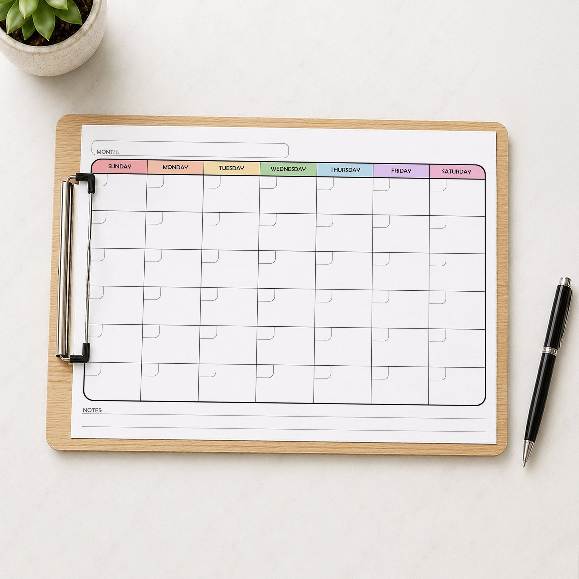 A printed rainbow undated monthly calendar (printable) page shown on a wooden clipboard on a table with a plant and a pen.